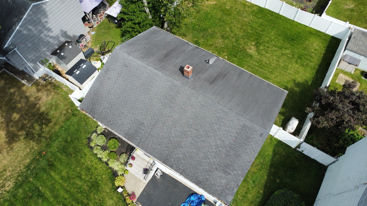 Overhead drone shot of a home with a GAF Pewter Gray asphalt shingle roof and brick chimney, securely installed against wind