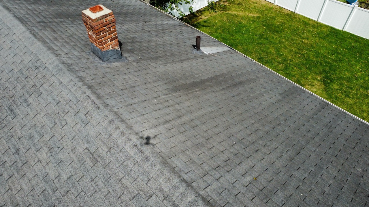 Red brick chimney and metal vent pipe rising above a gray asphalt shingle roof in New Jersey