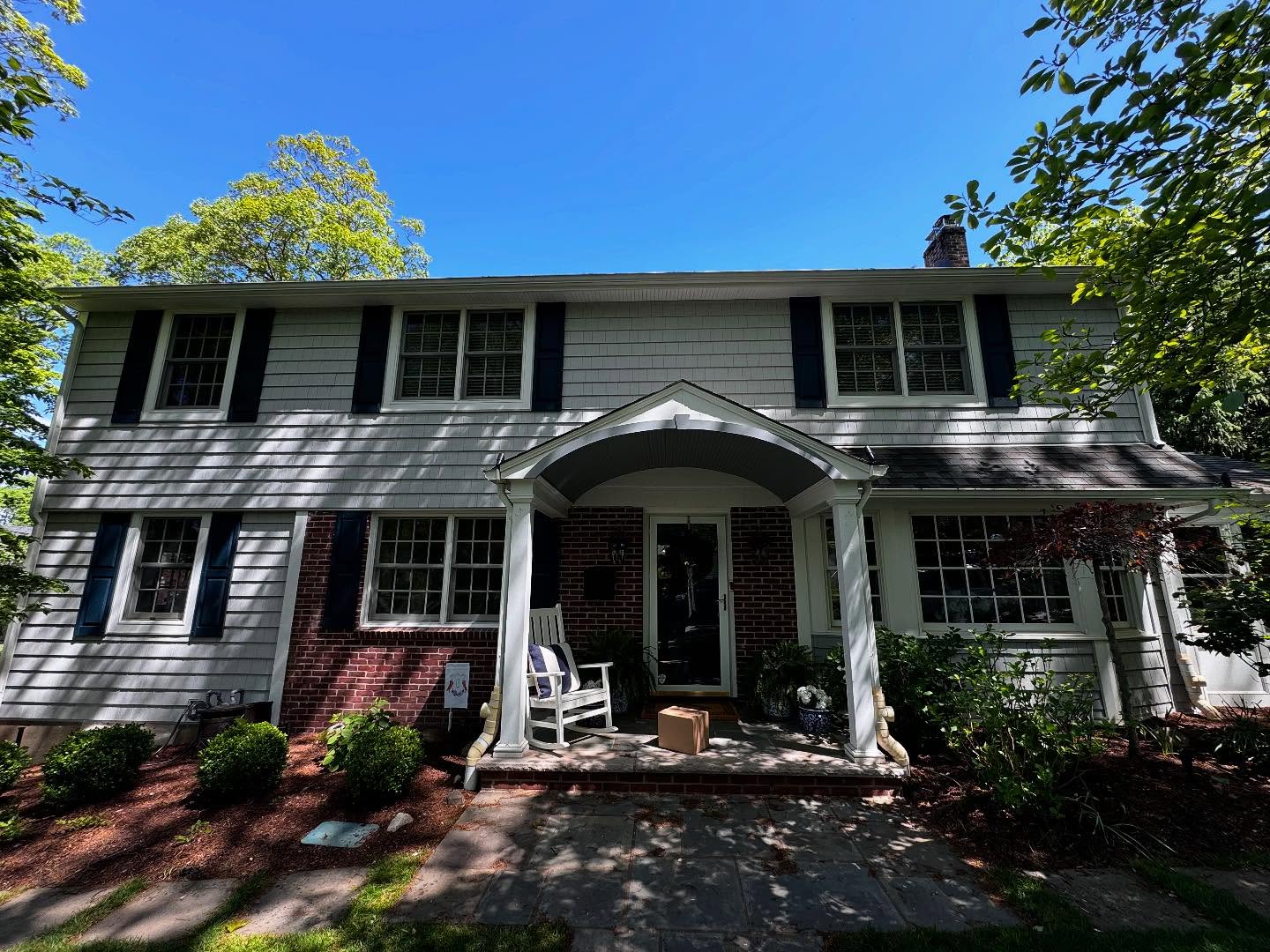 Colonial home with gray shingle siding, black shutters and a brick entryway portico