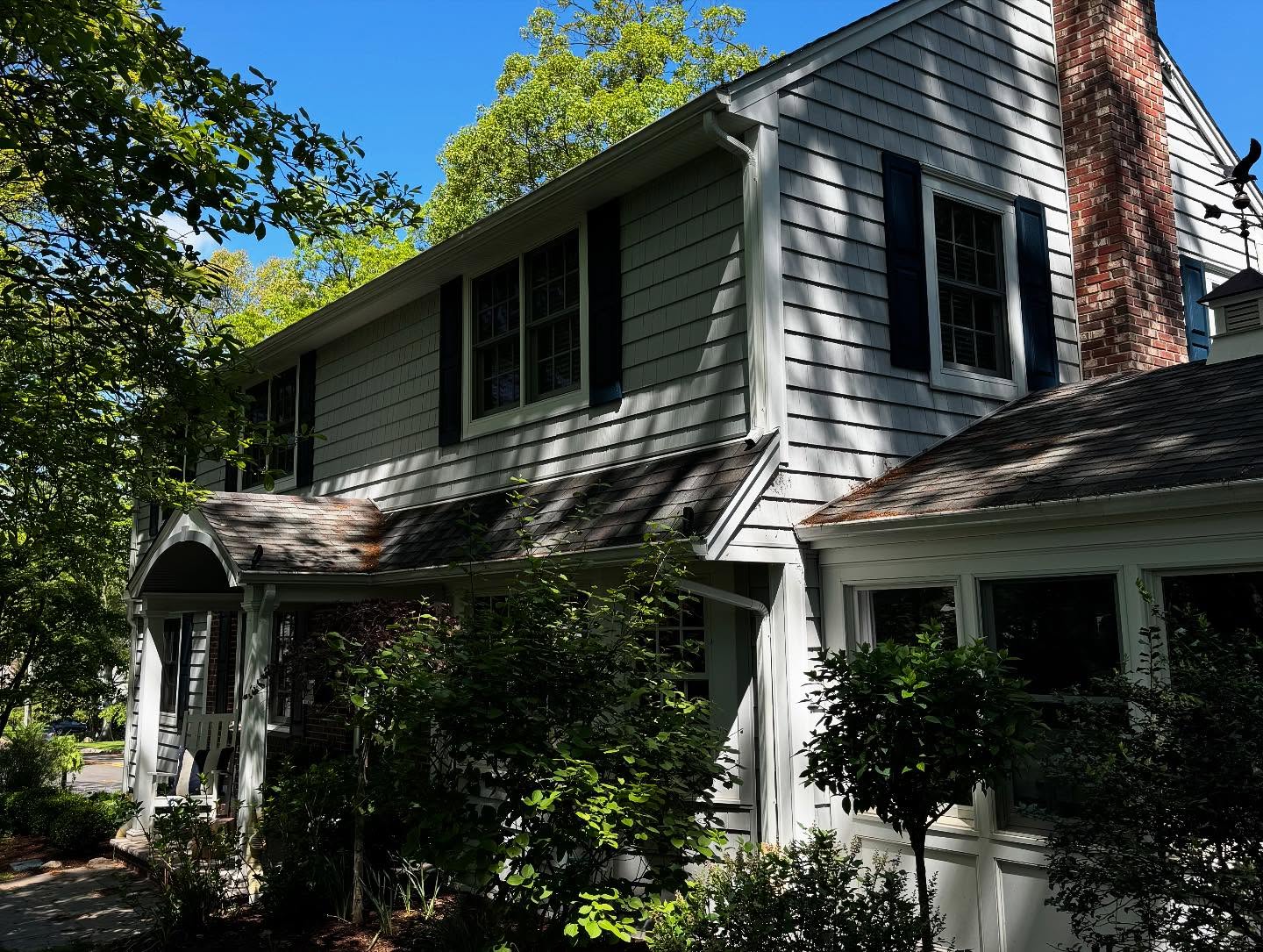 Two-story gray-shingled colonial with dark shutters, brick chimney and a covered porch