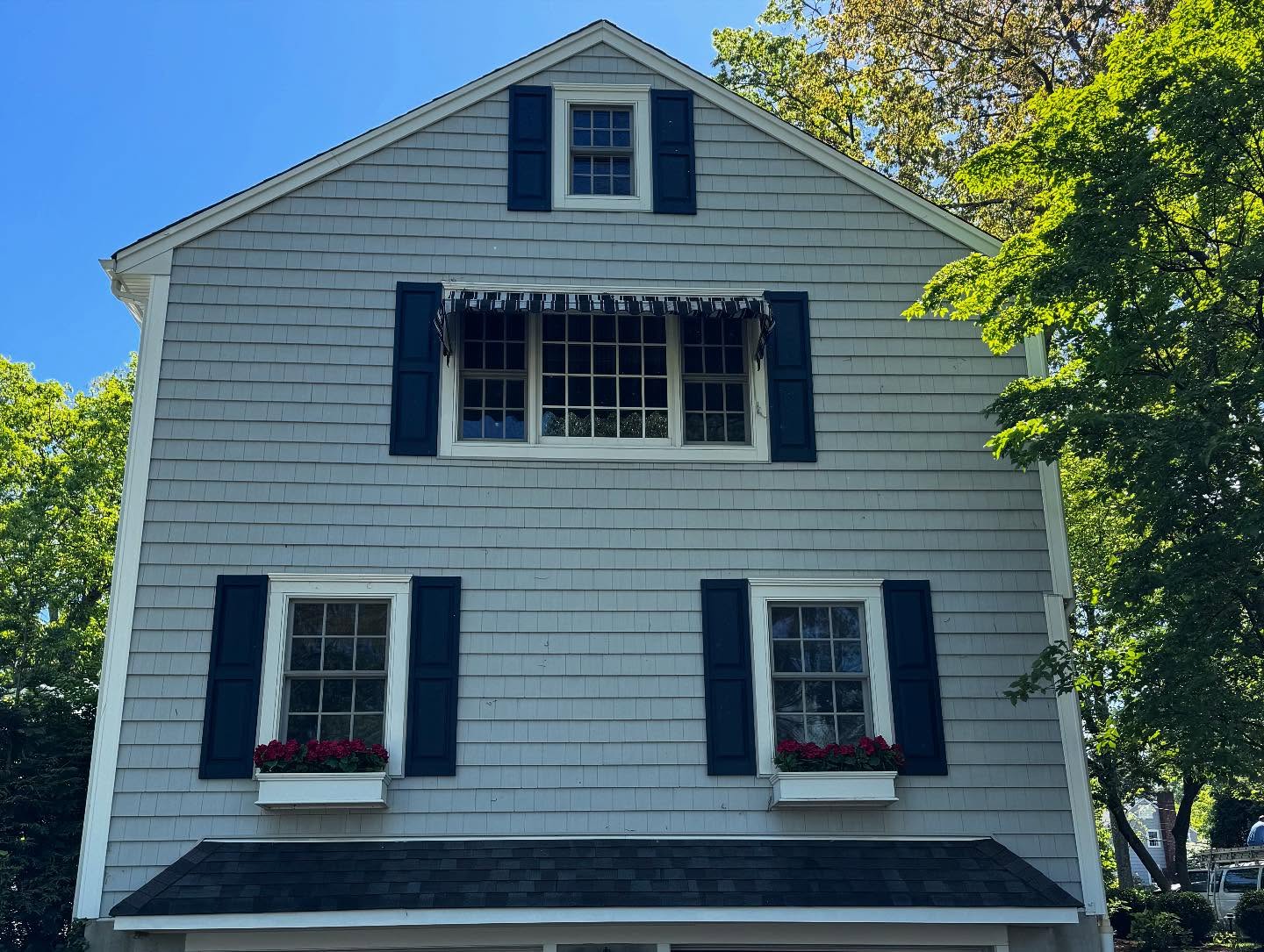 Gray shingled colonial facade with dark blue shutters, white window trim and red flower boxes