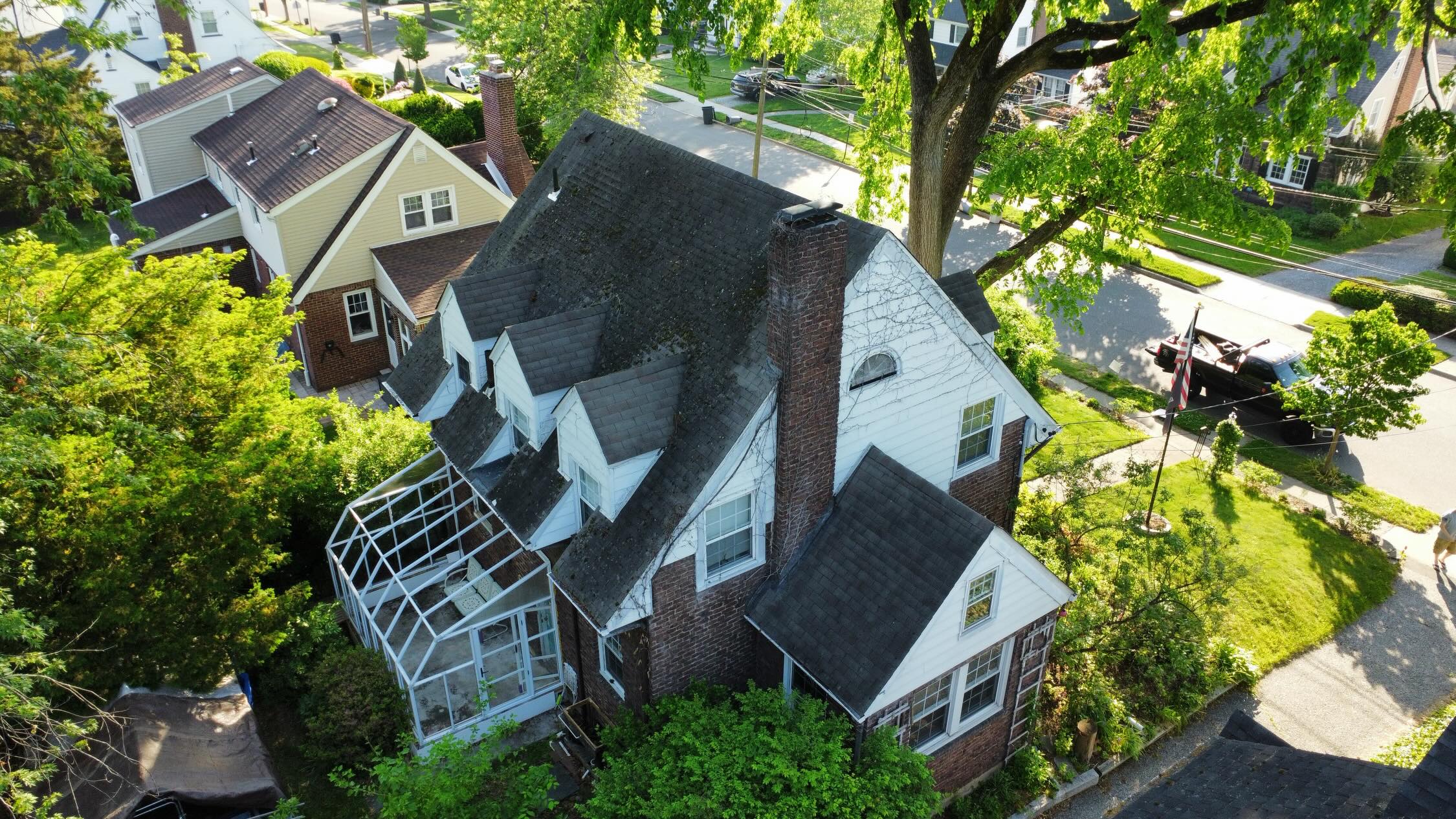 Aerial view of a brick New Jersey home with a complex shingled roof and two chimneys